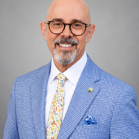 Alan Berg headshot in Blue jacket with white, floral print tie